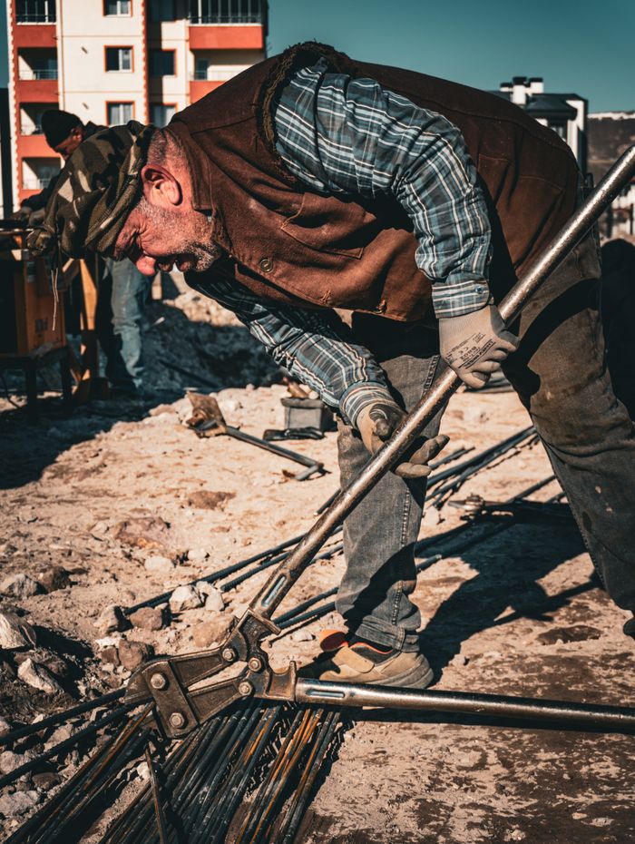 Senior man working on construction site in Türkiye, bending metal rods under sunny sky.